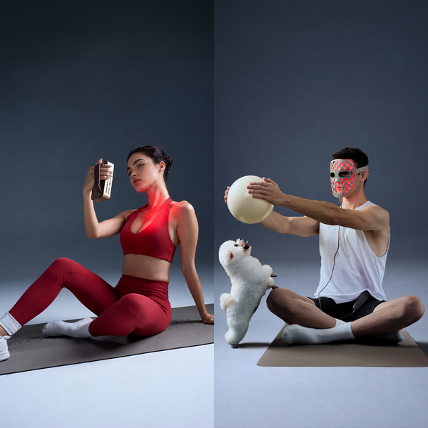 Woman in red activewear holds a device beside a masked man exercising with a ball and a small white dog.