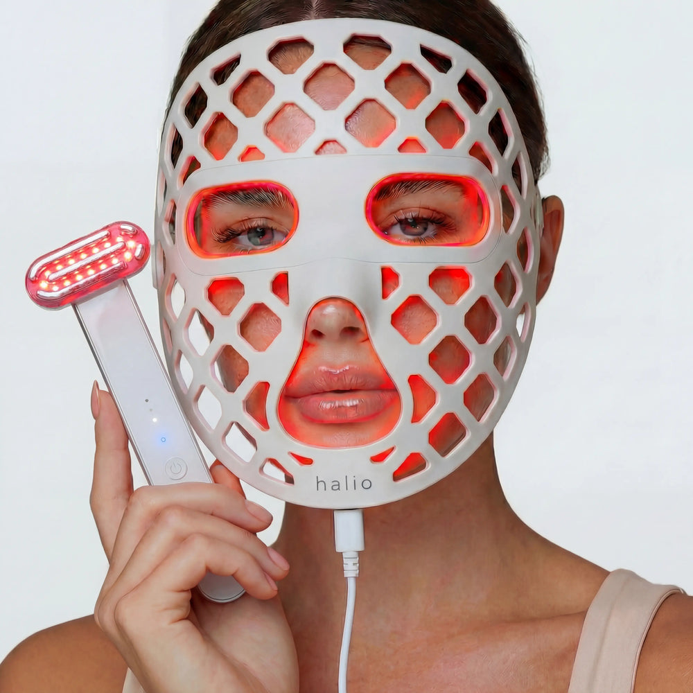 Person wearing a LED face mask with a handheld device, on a plain background