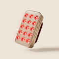 Halio RegenBoost handheld red light therapy panel with 15 glowing red LEDs and a metallic rose-gold finish.