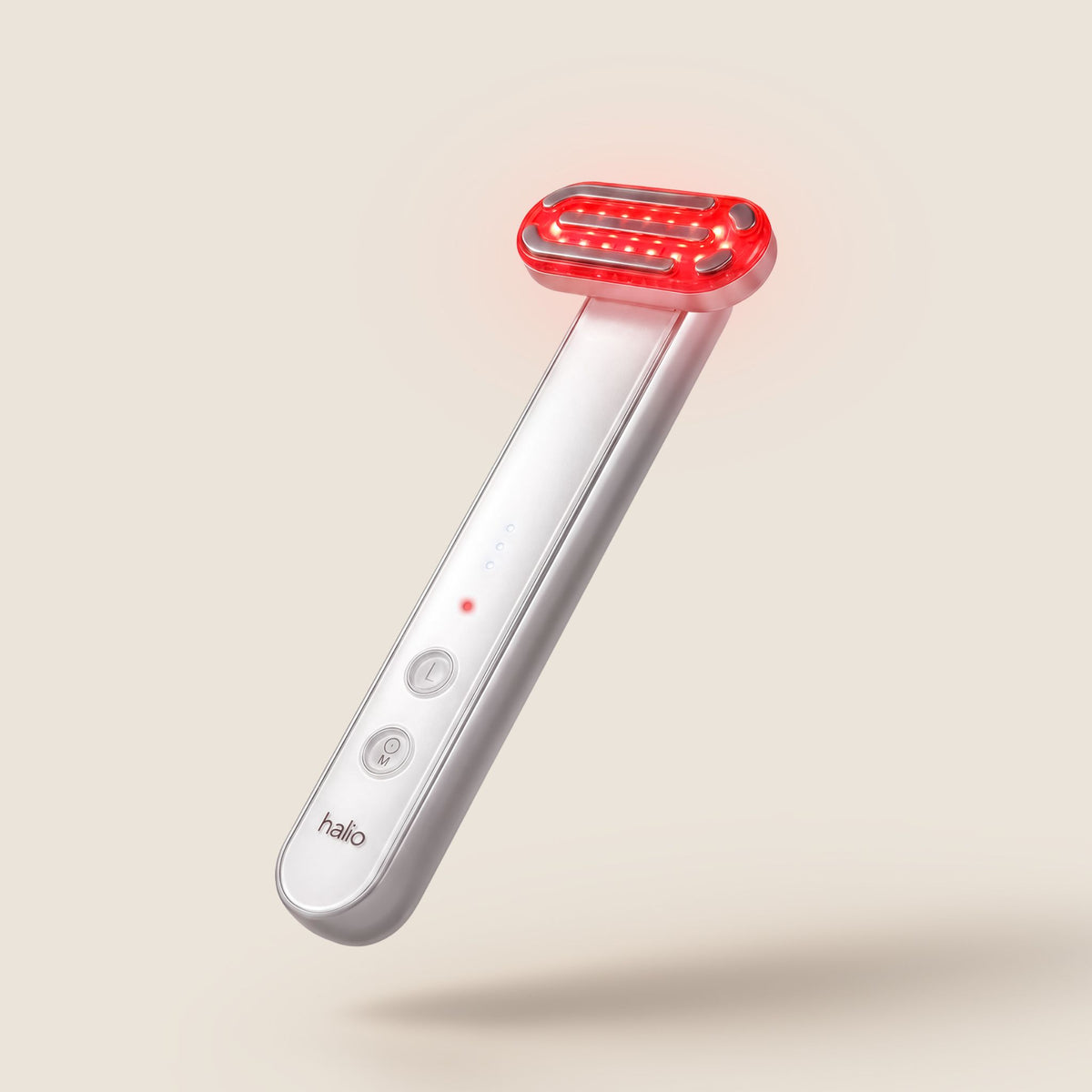 Halio handheld red light therapy wand with glowing red LED head and white handle, shown floating against a beige background